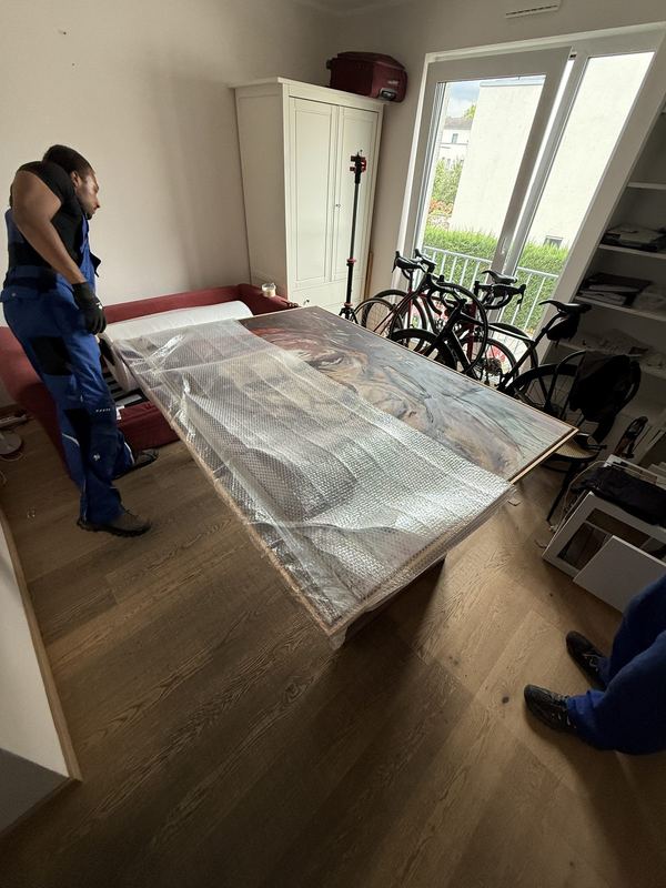 Ein großes Bild mit Rahmen liegt, in Luftpolsterfolie eingeschlagen, auf einem Tisch