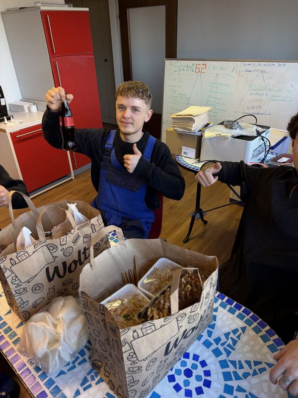 Ein Mitarbeiter mit Getränk hebt vor dem gemeinsamen Mittagessen den Daumen