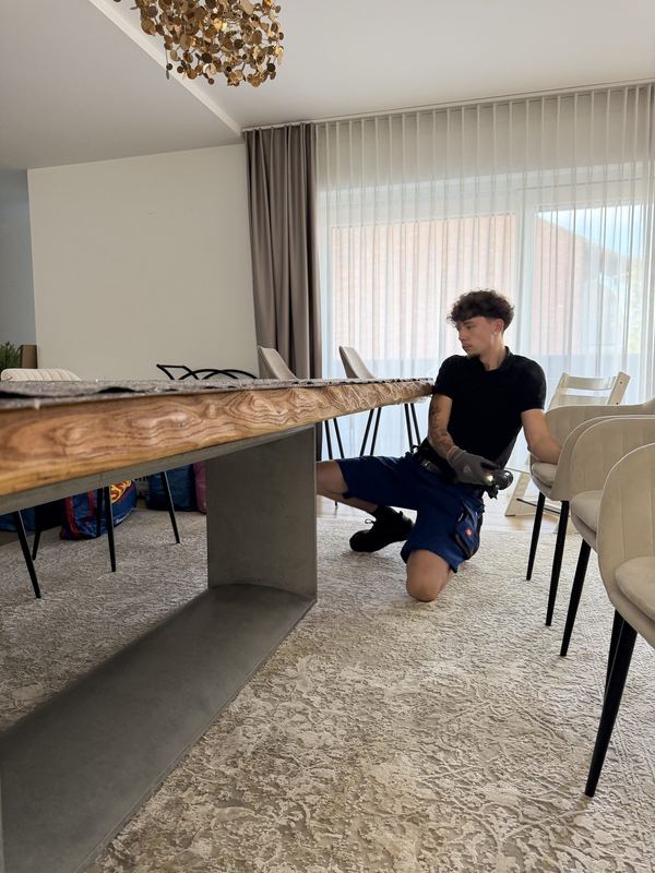 Ein Mitarbeiter kniet unter der Tischplatte und schraubt das Gestell fest