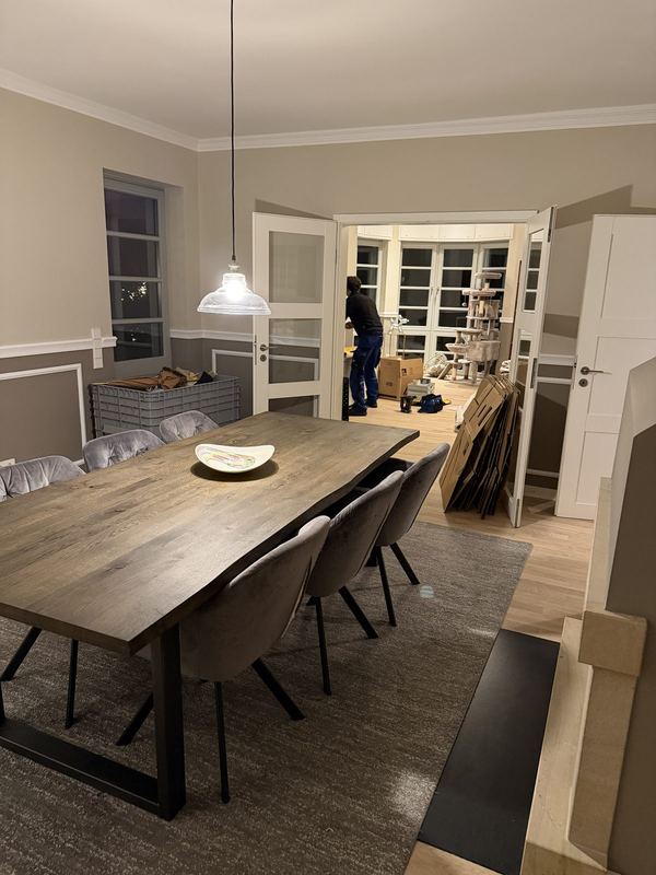 Ein fertig eingerichtetes Esszimmer, der Tisch ist gedeckt, im Raum daneben werden leere Kartons zusammengelegt