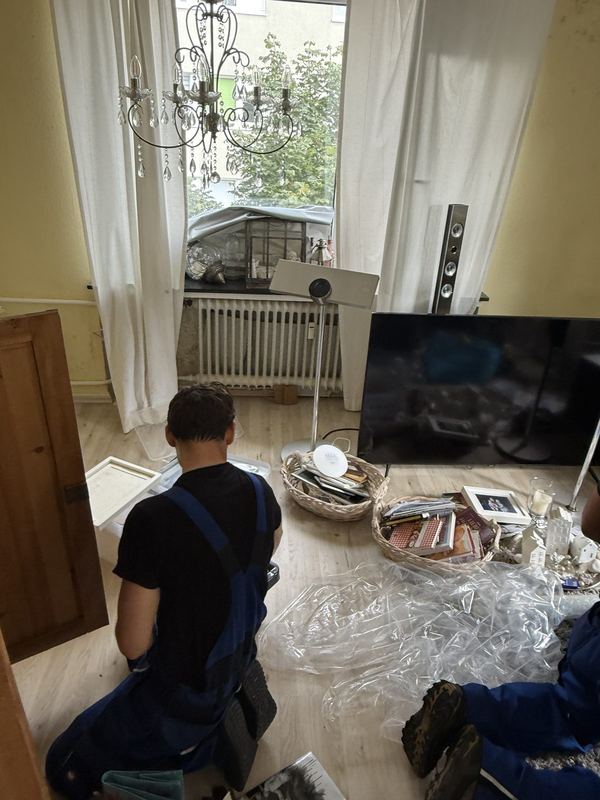 Auf dem Boden kniend sortiert ein Mitarbeiter Hausrat, der in Körben und Kisten liegt