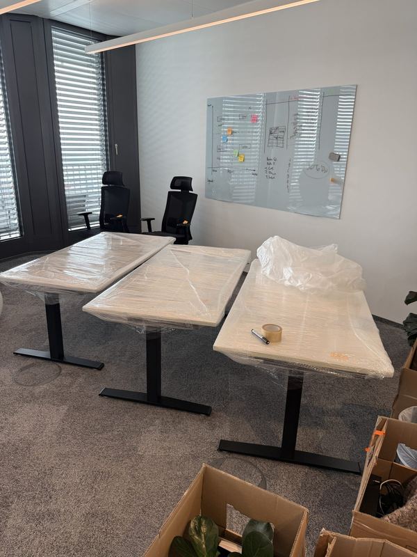 Drei nebeneinander stehende höhenverstellbare Schreibtische mit folierten Platten in einem Büro