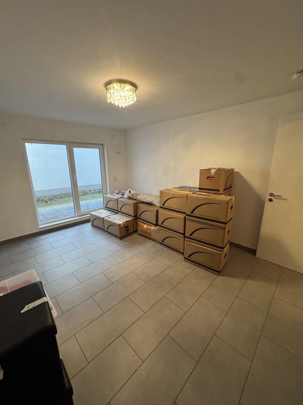 Aufeinandergestapelte Umzugskartons in einem noch leeren Zimmer eines Neubaus mit Fenster bis zum Boden