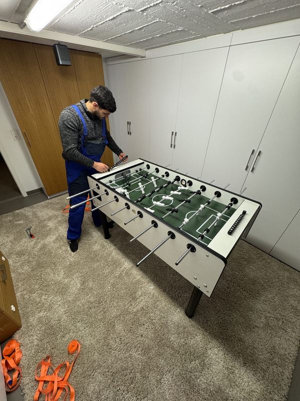 Ein Mitarbeiter montiert in einem Kellerraum die Spielstangen eines Tischkickers