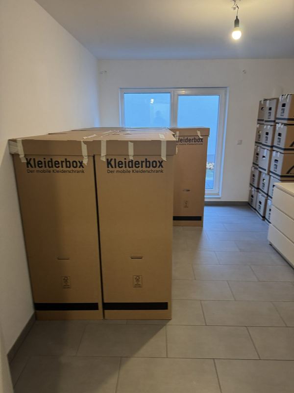 Ein leeres Zimmer, darin zwei Kleiderboxen und daneben aufgestapelte Umzugskartons