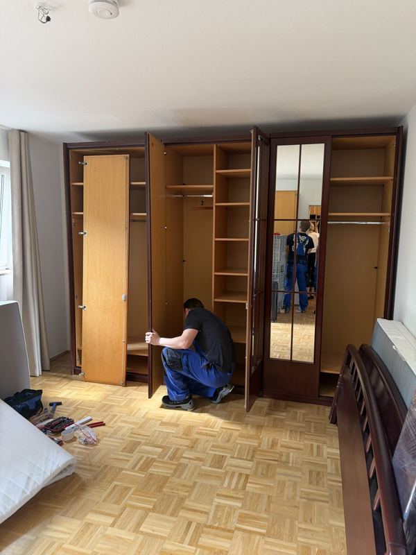 In einem Schlafzimmer justiert ein Mitarbeiter die Türen eines Kleiderschranks mit mehreren Türen
