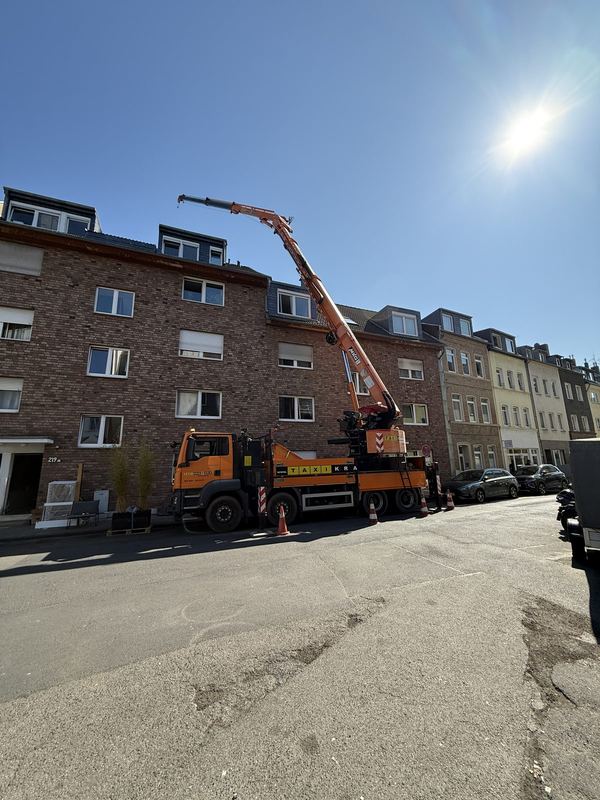 Warnkegel sichern einen orangefarbenen Kranwagen ab, dessen Ausleger in einer Wohnstraße ausgefahren ist