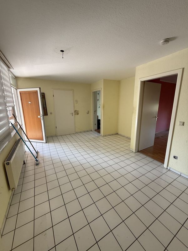 Zimmer nach dem Einsatz, ausgeräumt Leergeräumtes Zimmer mit gelb gestrichenen Wänden, weißen Bodenfliesen, einem Heizkörper und geöffneten Türen