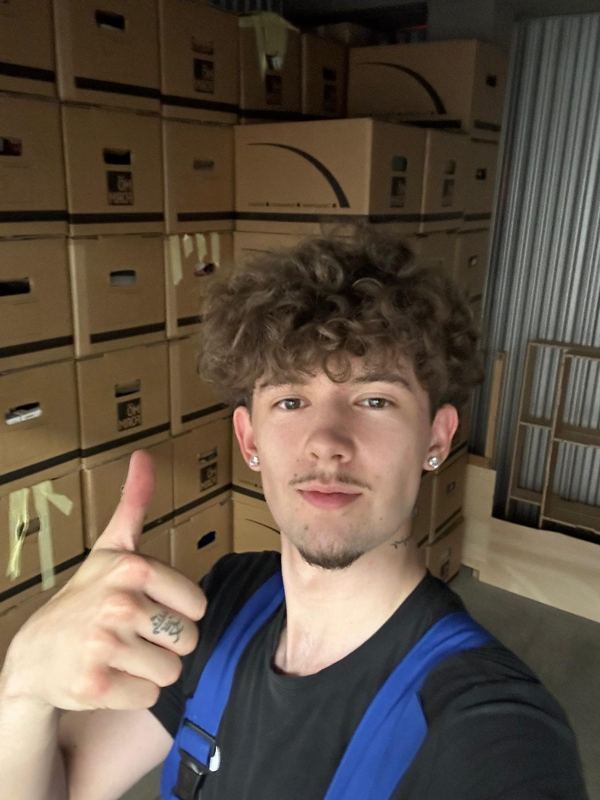 Ein Mitarbeiter vor einer Wand aus gepackten, beschrifteten Umzugskartons