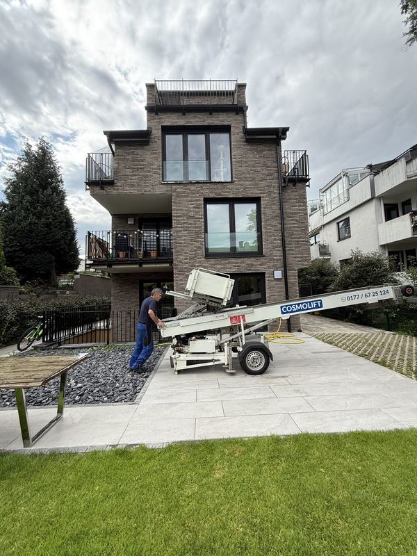 Auf der Einfahrt vor einem Wohnhaus richtet ein Mitarbeiter einen Möbellift aus