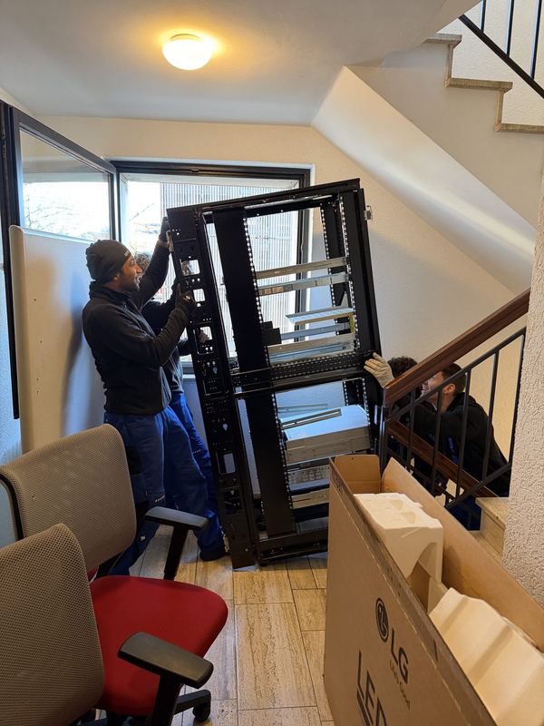 Drei Mitarbeiter bringen einen offenen Serverschrank die Treppe hinunter