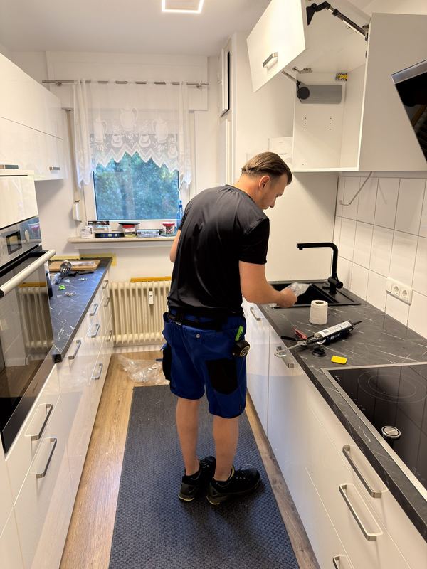 Ein Mitarbeiter lässt die schwarze Spüle in den passenden Ausschnitt der Arbeitsplatte ein