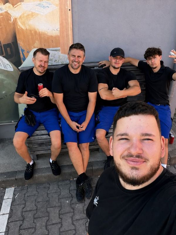 Das Team in Arbeitskleidung sitzt in der Pause gemeinsam auf einer Bank in der Sonne
