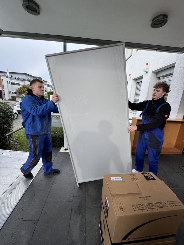Zwei Mitarbeiter bringen eine große weiße Platte hochkant zum Fahrzeug