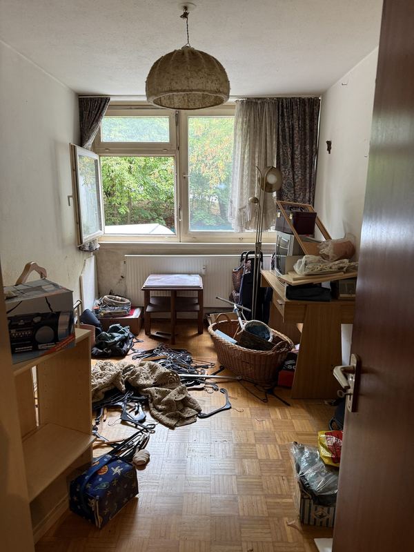 Ein Zimmer vor der Räumung mit Kleiderbügeln, Körben und Kartons auf dem Boden