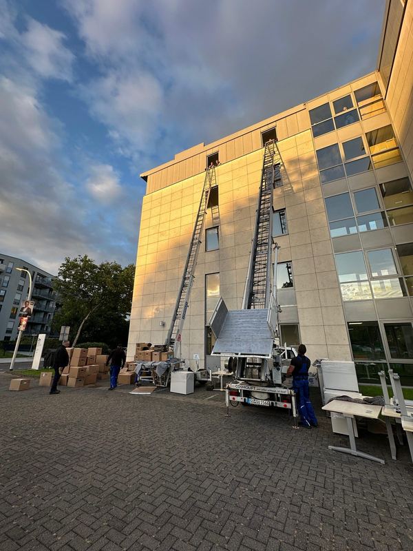Vor der Fassade eines Bürogebäudes stehen zwei ausgefahrene Möbellifte Seite an Seite